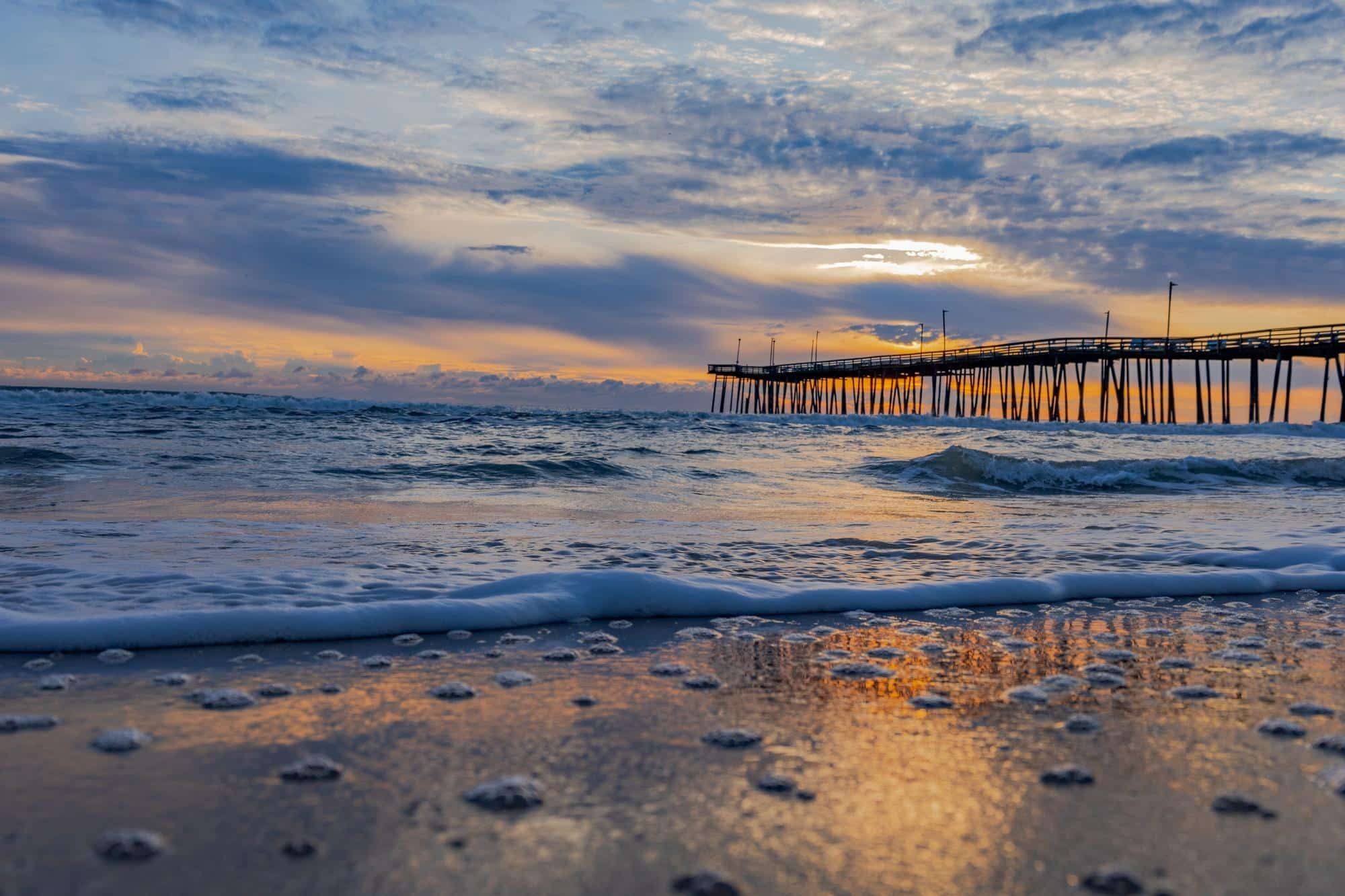 A beach with waves and a pier.