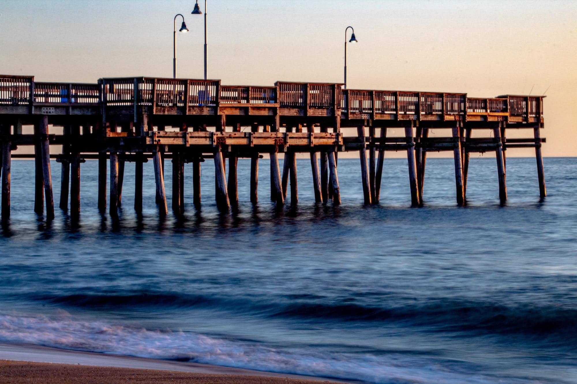 A fishing pier on the beach with waves in the water.