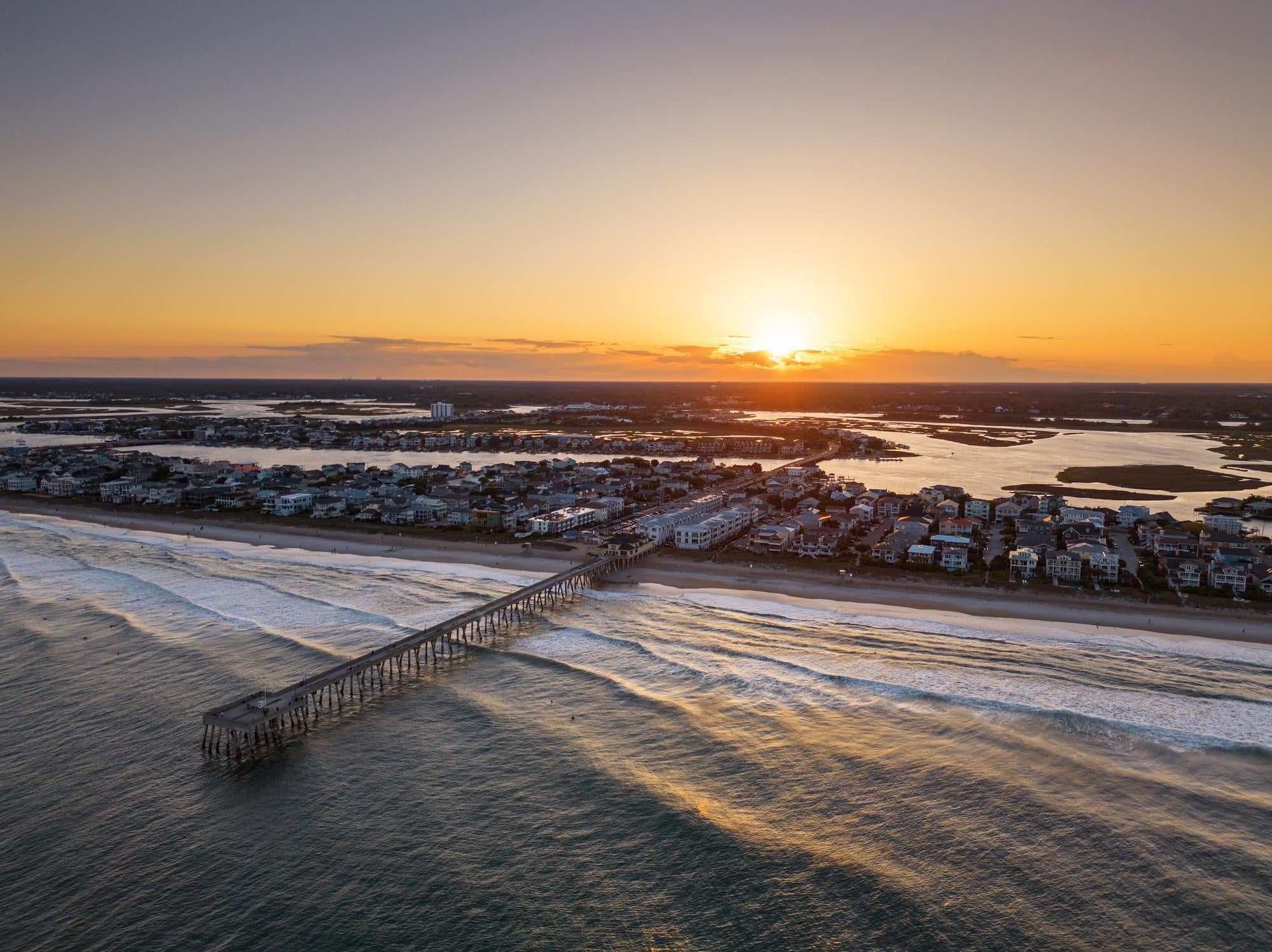 An aerial shot over a fishing pier on a beach town during sunrise.